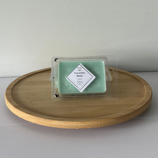 Green wax melt in a clear container on a wooden tray against a light gray background